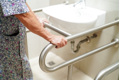 Personne en perte de mobilité qui se tient à une barre murale dans sa salle de bain.